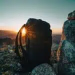 Mochila de senderismo al amanecer en lo alto de una montaña, con el sol saliendo entre las asas.