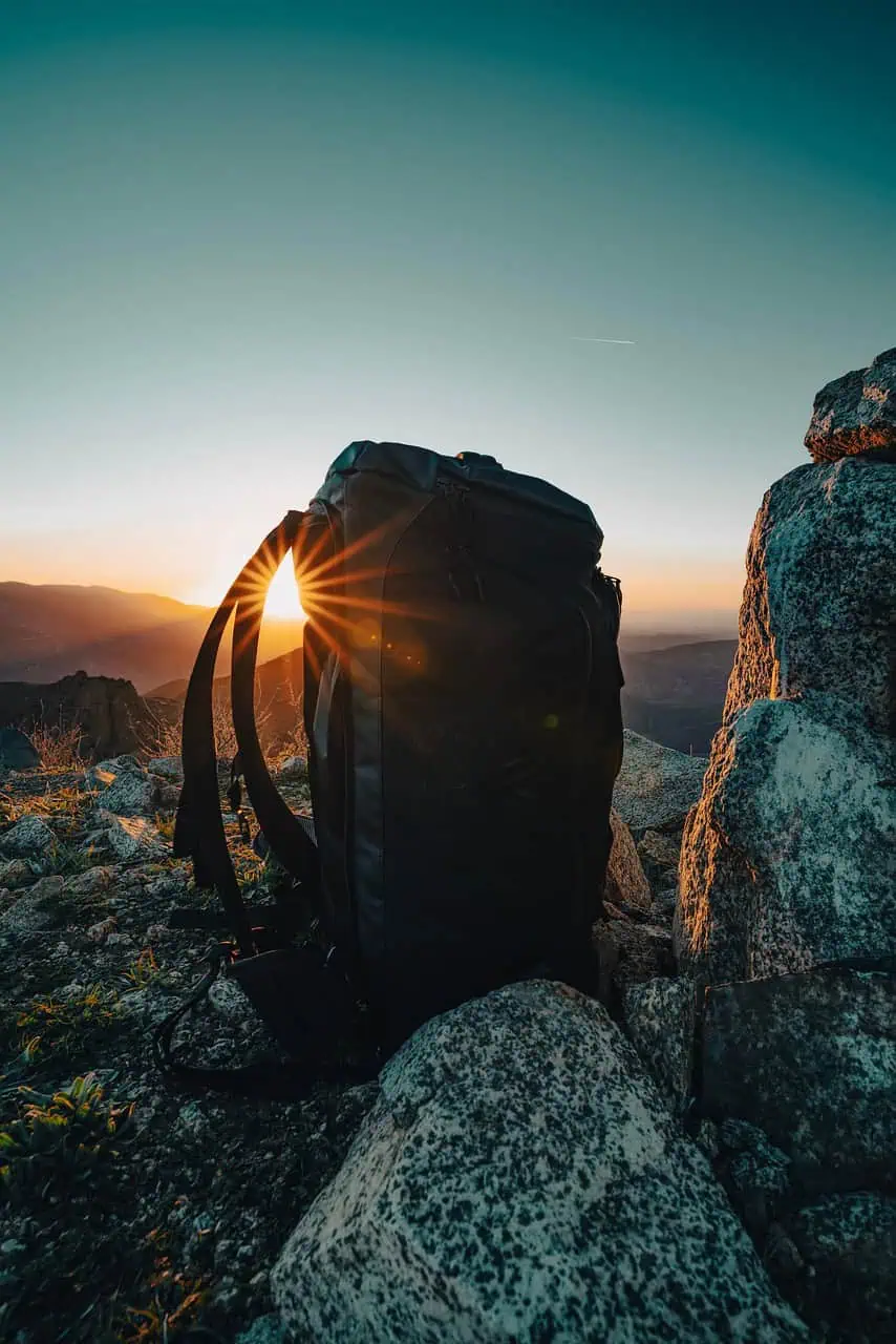 Mochila de senderismo al amanecer en lo alto de una montaña, con el sol saliendo entre las asas.