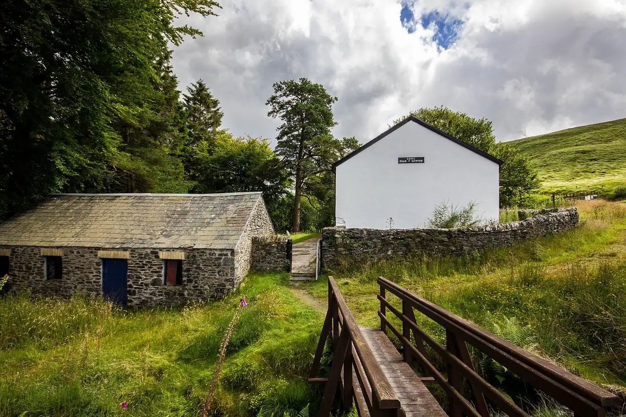 Casa rural blanca y edificio de piedra junto a un pequeño puente de madera en una aldea verde del Camino, rodeada de naturaleza y silencio